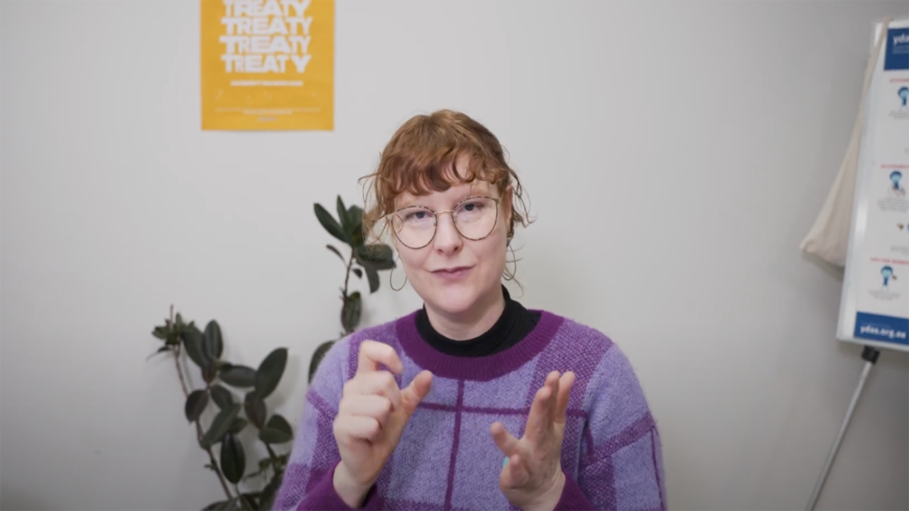 Photo of a white person in an office, signing in Auslan